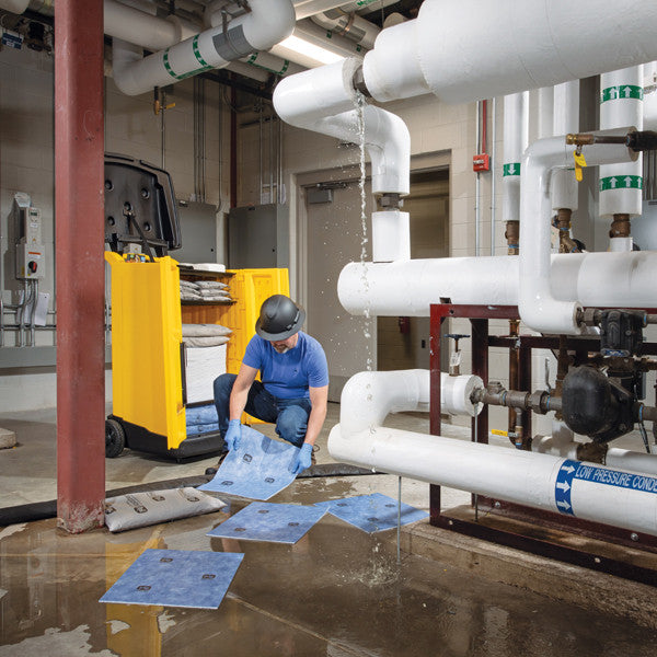 Medewerker gebruikt waterabsorberende spill kit op wielen in gele container om lekkage bij buizen in fabriek op ruimen
