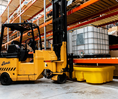 Gele lekbak onder palletrek in gebruik in een magazijn, met een IBC-container op het rek en een heftruck ernaast