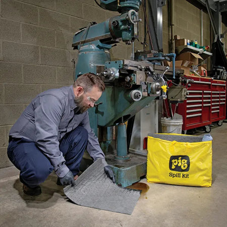Monteur gebruikt de absorberende mat uit de universele spill kit van absorptieshop na olielekkage in de werkplaats