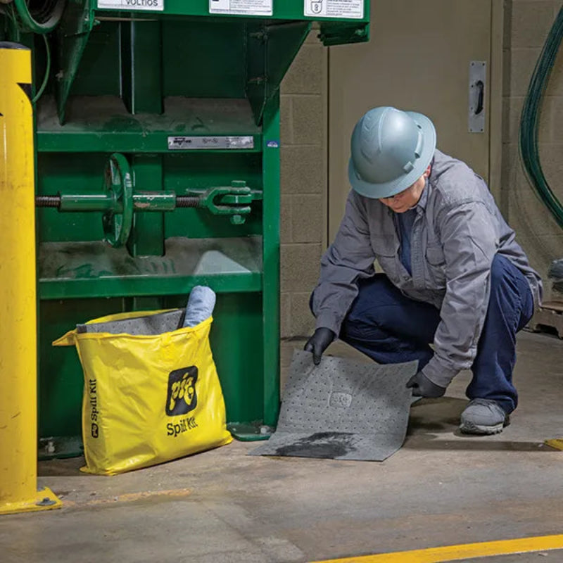 Medewerker gebruikt absorberende mat uit de universele spill kit van absorptieshop na lekkage bij industriële machine in de werkplaats